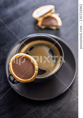 Sweet chocolate tartelettes and coffee cup on black table. Sweet chocolate tartelettes and coffee cup on black table. 130728962