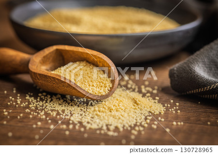 Uncooked couscous on wooden scoop on wooden table. 130728965