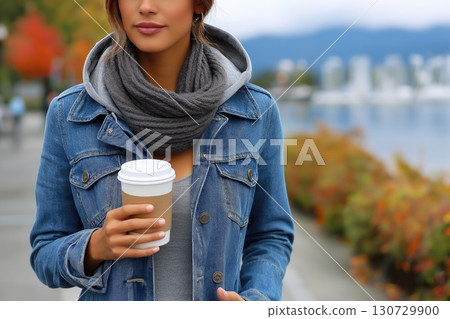 Young woman holding coffee walking in autumn day outdoors by the sea 130729900