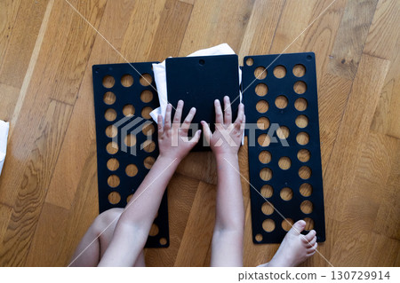Child folding clothes with black plastic flip folder on wooden floor 130729914