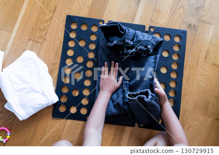 Child learning laundry folding with black garment organizer on wooden floor Child learning laundry folding with black garment organizer on wooden floor 130729915