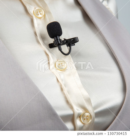 A black lavalier microphone with a clip is attached to a cream-colored button-up shirt 130730415