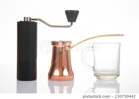A modern black manual coffee grinder paired with a traditional copper cezve 130730442