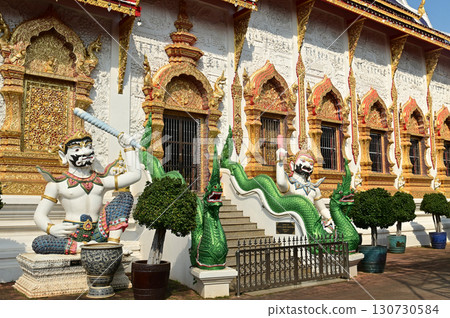 Statues of sitting white Giant holding a baton in Thai art, decorate the front of the Church or Chapel at Wat Den Sali Si Mueang Kaen temple. Located at Chaing Mai Province in Thailand. Statues of sitting white Giant holding a baton in Thai art, decorate the front of the Church or Chapel at Wat Den Sali Si Mueang Kaen temple. Located at Chaing Mai Province in Thailand. 130730584