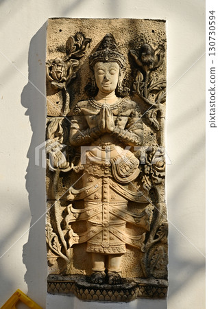 A Thai art statue of an angel in a standing position with hands together, decorated on the side wall of the chapel in the temple area at Wat Den Sali Si Mueang Kaen temple. A Thai art statue of an angel in a standing position with hands together, decorated on the side wall of the chapel in the temple area at Wat Den Sali Si Mueang Kaen temple. 130730594