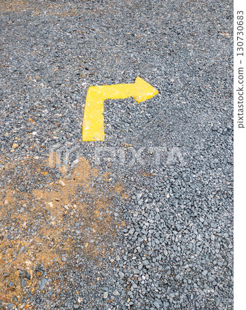 Faded Yellow Directional Arrow on Gravel. 130730683