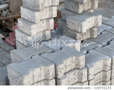 Grey concrete interlocking paving stones stacked outdoors. Construction materials for building roads, driveways, or garden paths. Textured surface, ready for installation. Grey concrete interlocking paving stones stacked outdoors. Construction materials for building roads, driveways, or garden paths. Textured surface, ready for installation. 130731172