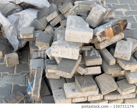 Large pile of grey concrete paving blocks and bricks. Assorted rough textured building materials stacked outdoors on a paved surface. Large pile of grey concrete paving blocks and bricks. Assorted rough textured building materials stacked outdoors on a paved surface. 130731174