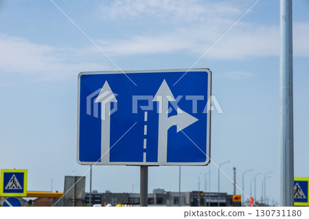 Blue rectangular road sign featuring white straight and right turn arrows providing directions under a bright sky. Blue rectangular road sign featuring white straight and right turn arrows providing directions under a bright sky. 130731180