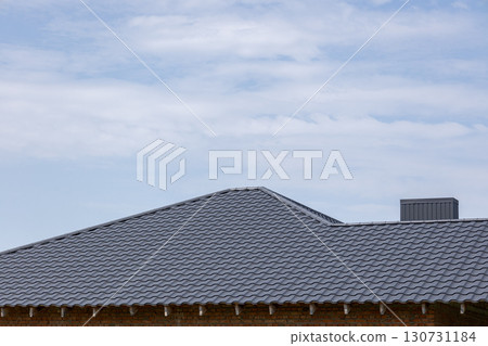 New modern gray tiled roof and chimney on a brick building under a bright blue sky with light white clouds. 130731184