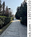 Sunlit stone pathway leads through landscaped garden with evergreen trees and blue sky in background, peaceful outdoor nature, walking, and scenic park landscape concept 130731350