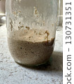 Active sourdough starter with visible bubbles and organic texture in glass jar, homemade fermentation, rustic kitchen baking, healthy bread preparation, and artisanal food concept 130731351
