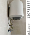 Wall-mounted electric water heater with exposed metal pipes and safety wires, modern bathroom appliance installation, plumbing, maintenance, and home repair concept 130731357
