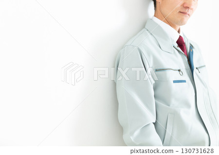A middle-aged male businessman in work clothes leaning against a white wall 130731628