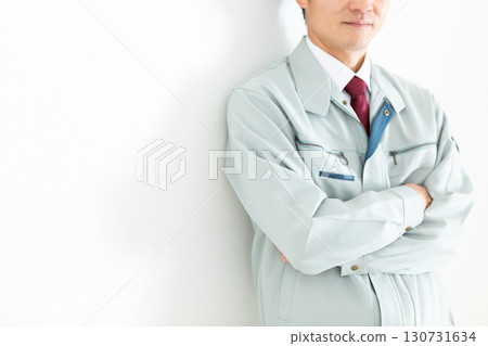 A middle-aged male businessman in work clothes leaning against a white wall 130731634