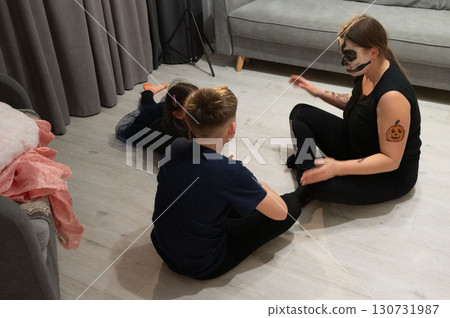 A woman with Halloween face paint plays with two children on the floor. A woman with Halloween face paint plays with two children on the floor. 130731987