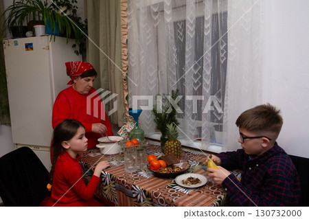 Grandma prepares food while her grandchildren enjoy a snack at the kitchen table. 130732000
