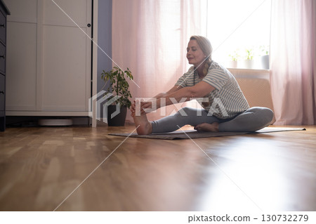 40-year-old woman doing yoga at home, stretching and hip-opening exercises 40-year-old woman doing yoga at home, stretching and hip-opening exercises 130732279