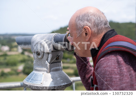 elderly man looking through tourist viewing telescope at fortress in Portugal elderly man looking through tourist viewing telescope at fortress in Portugal 130732320