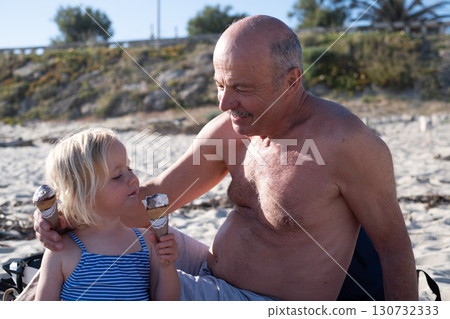 European girl eating ice cream on the beach with her grandfather European girl eating ice cream on the beach with her grandfather 130732333