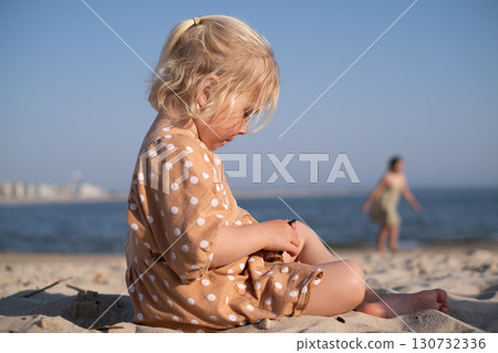 blonde girl sitting on the beach and playing alone blonde girl sitting on the beach and playing alone 130732336