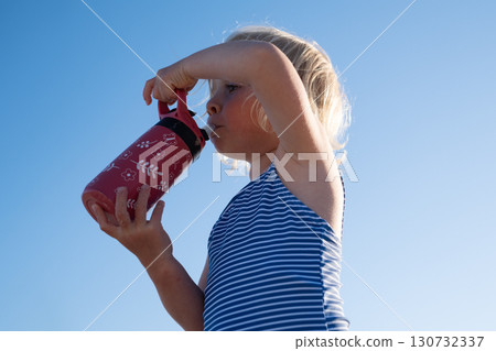 European blonde girl in swimsuit drinking water on a hot summer day, hydration 130732337
