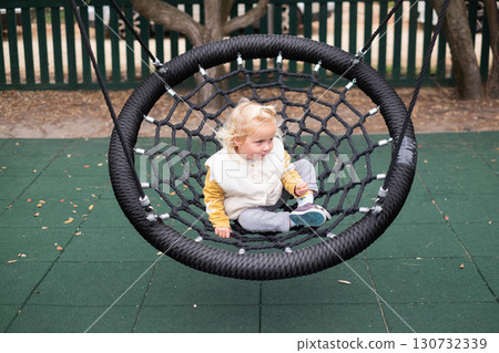 little European girl swinging on a swing at the playground little European girl swinging on a swing at the playground 130732339