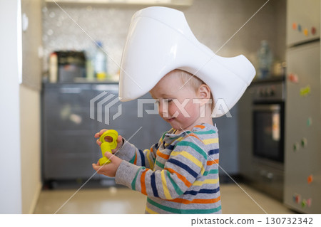 European toddler girl put a potty on her head like a hat and plays with toy, potty training 130732342