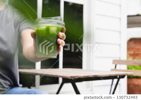 Woman reaching hand with glass of iced Matcha green tea to camera. 130732493