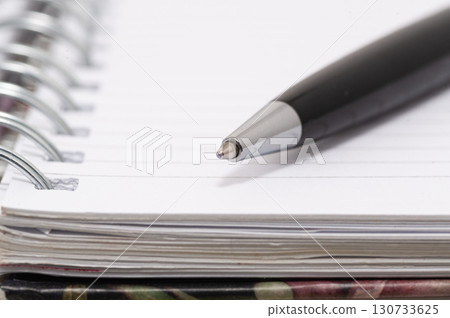 A pen is sitting on a spiral bound notebook 130733625