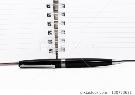 A black pen is on a white page of a spiral bound notebook 130733681