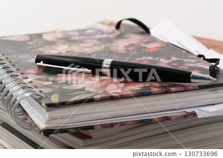 A black pen is on top of a spiral bound notebook 130733696