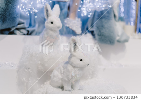 Two white rabbits are sitting on a snow pile 130733834