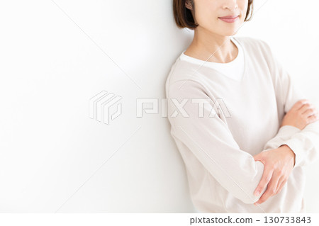 A middle-aged woman in casual clothes leaning against a white wall by the window A middle-aged woman in casual clothes leaning against a white wall by the window 130733843