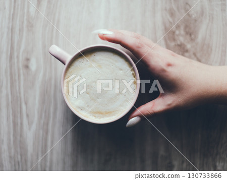 A hand holding a cup of coffee on a wooden table 130733866