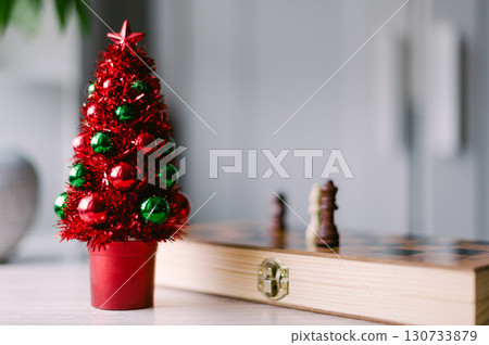 A red and green Christmas tree sits on a table next to a chess set 130733879