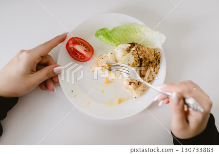 A person is eating a plate of food with a fork 130733883