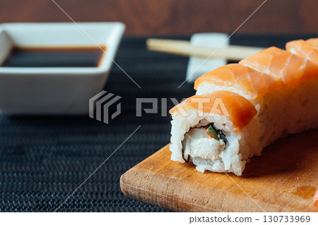 A sushi roll with a sauce on a wooden cutting board A sushi roll with a sauce on a wooden cutting board 130733969