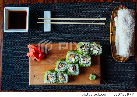 A plate of sushi with chopsticks and a small bowl of sauce 130733977