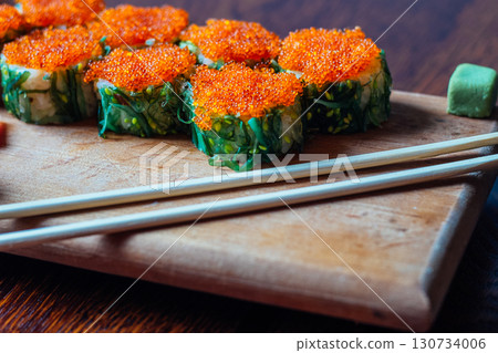 A plate of sushi with orange sauce and green seaweed 130734006