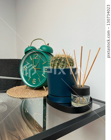 A green alarm clock sits on a table next to a small plant 130734023