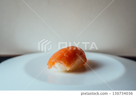 A piece of sushi is sitting on a white plate 130734036