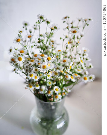 A vase of white and yellow flowers sits on a white table 130734062