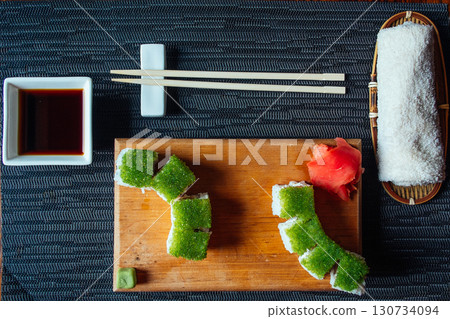 A plate of sushi with green seaweed and a small bowl of sauce 130734094