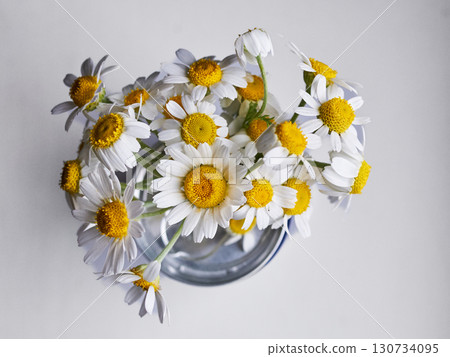 A vase of white and yellow flowers sits on a white table A vase of white and yellow flowers sits on a white table 130734095