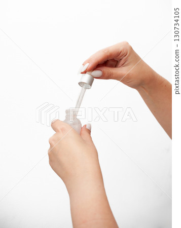 A person is holding a bottle of liquid and pouring it into their hand 130734105