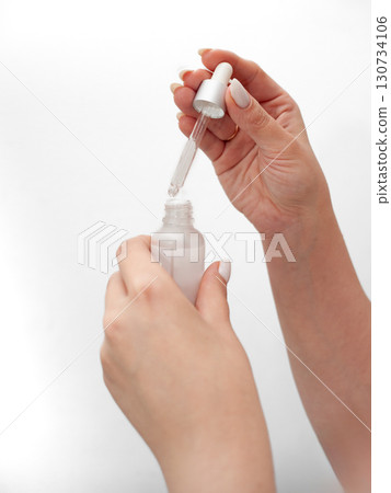 A woman is holding a bottle of perfume and is about to spray it on her wrist A woman is holding a bottle of perfume and is about to spray it on her wrist 130734106