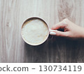 A hand holding a cup of coffee on a wooden table 130734119
