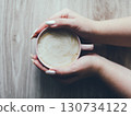 A hand holding a cup of coffee on a wooden table 130734122