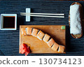 A sushi roll sits on a wooden cutting board with chopsticks and a napkin nearby 130734123